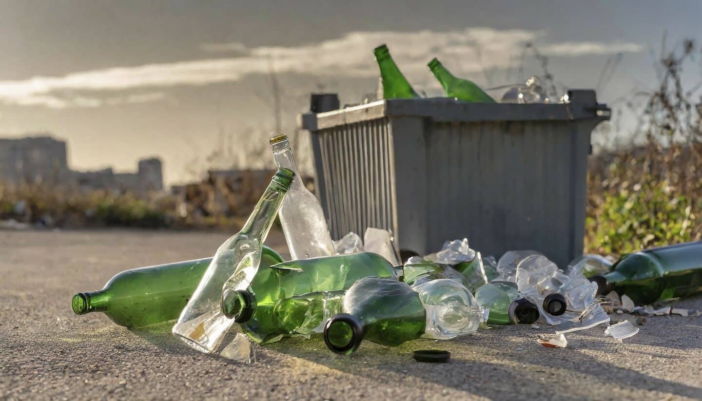 Bouteilles en verre cassé sur le sol et dans une poubelle en extérieur